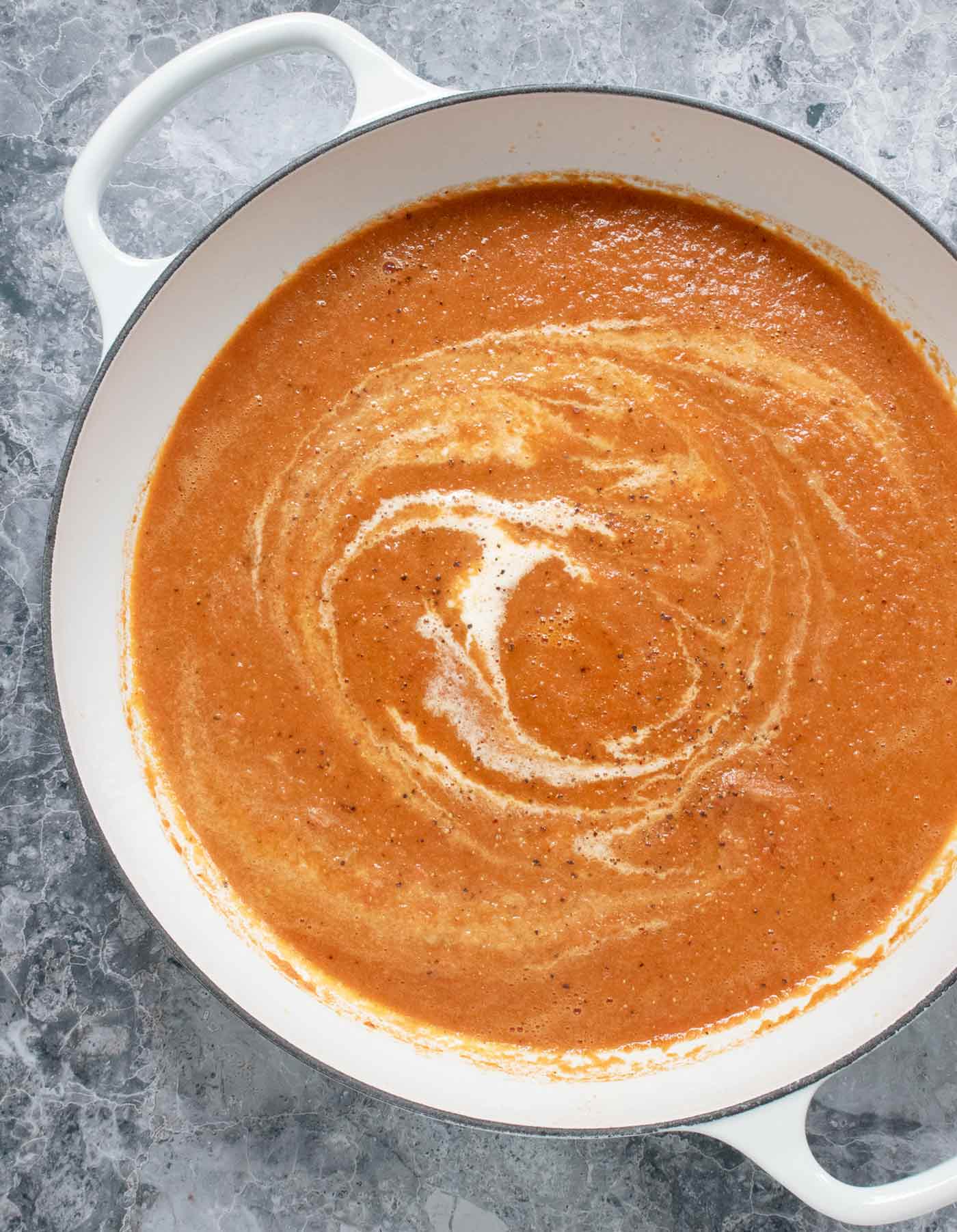 Overhead view of Air Fryer Roasted Tomato Soup in the pan, with swirls of heavy cream.