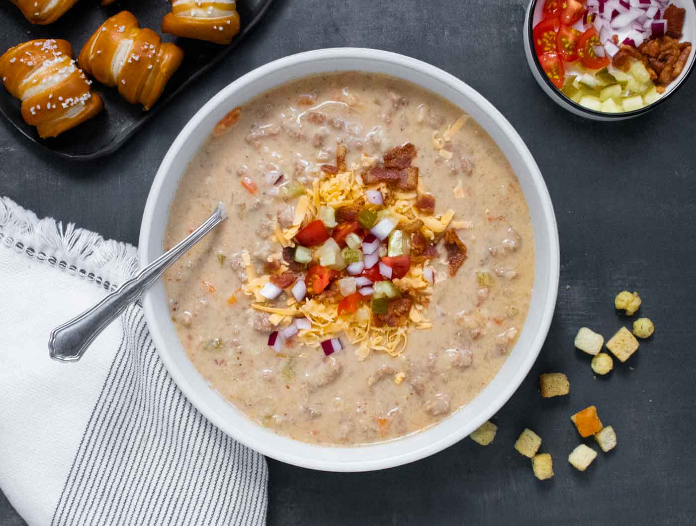 Overhead view of Cheeseburger Beer Soup in a bowl with a spoon and toppings on the side.