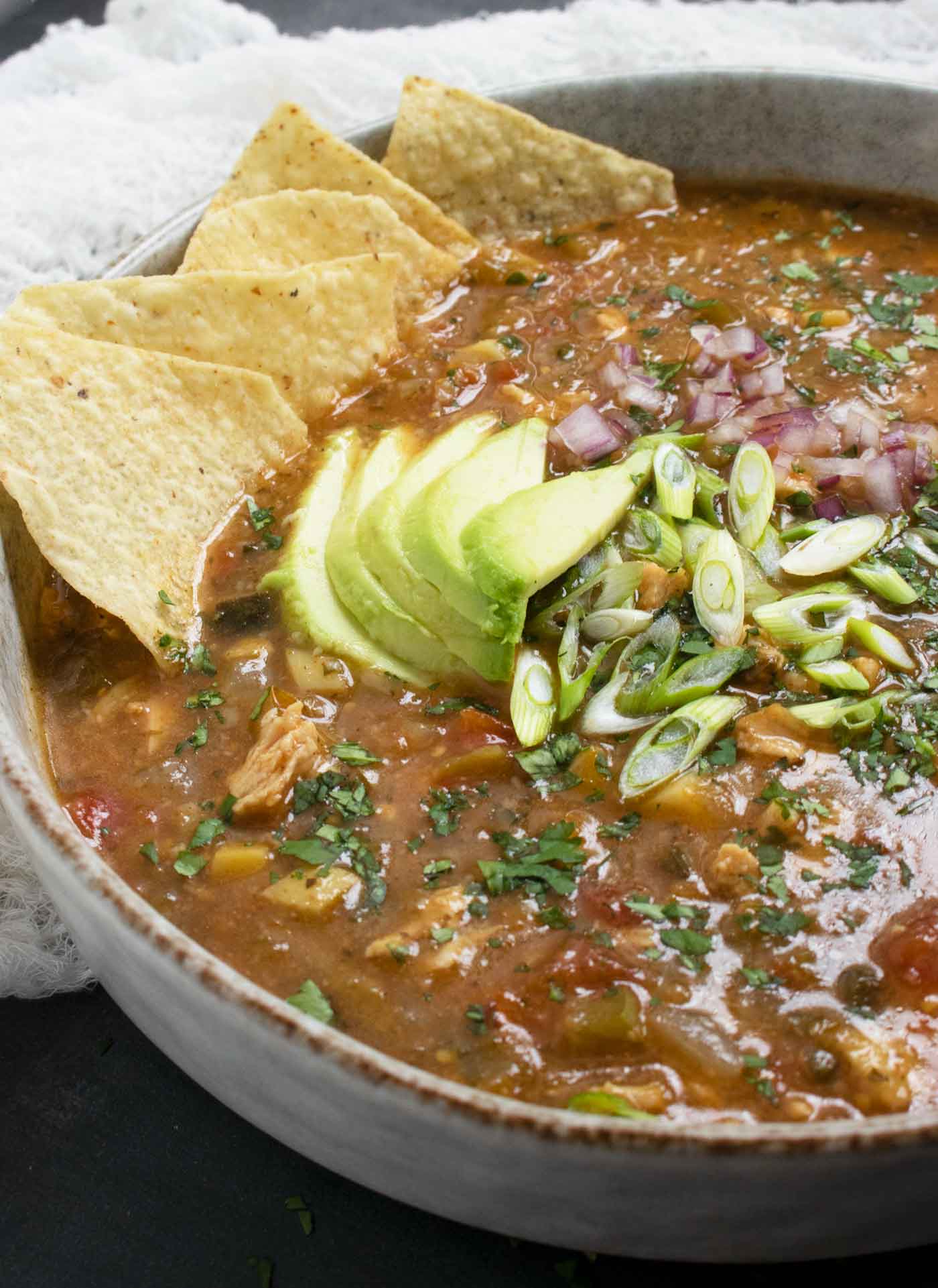 Side-angled, close-up view of a bowl of Chile Verde Tortilla Soup with lots of toppings.