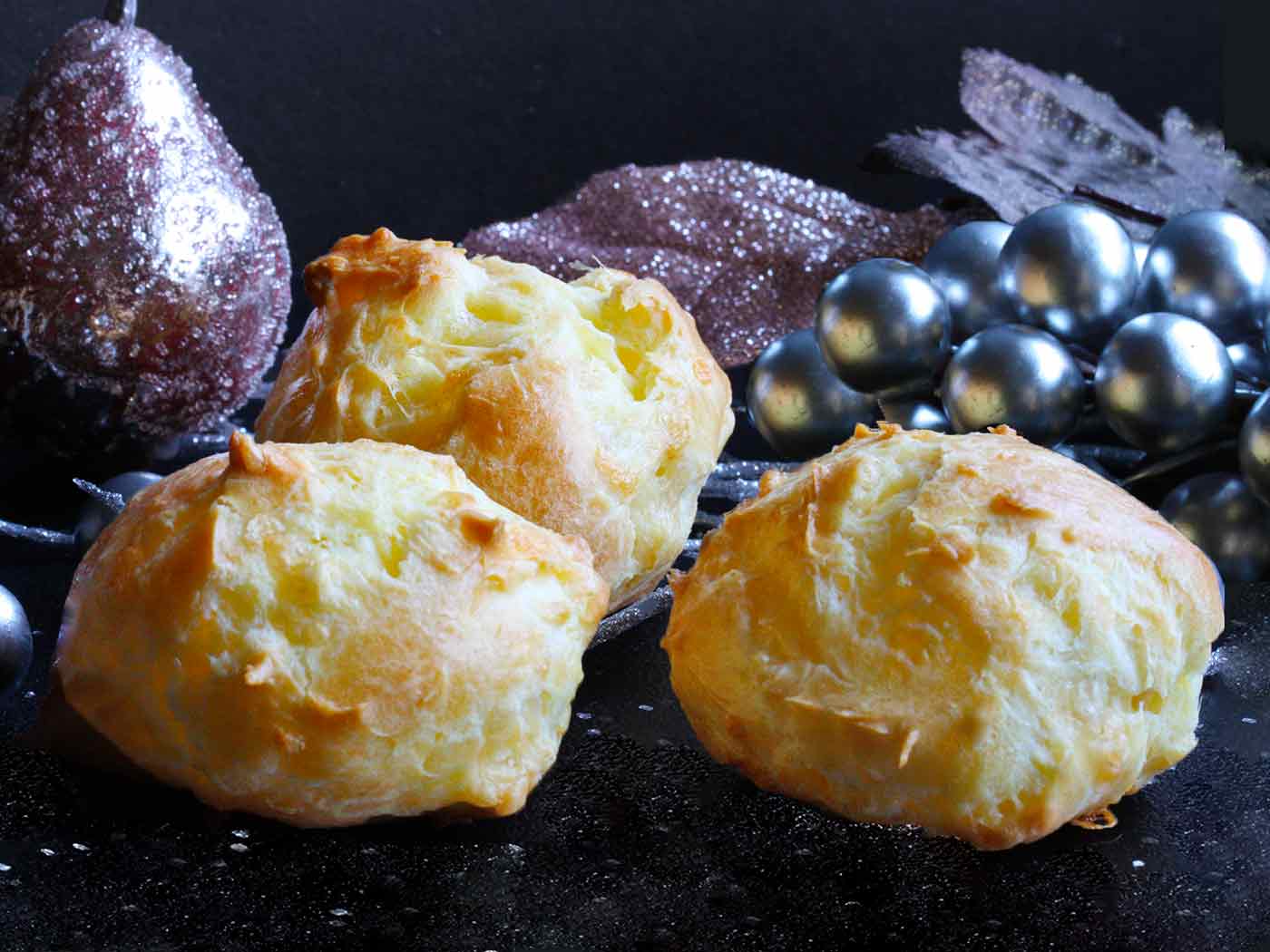Three gougeres on a dark board with Christmas decorations.