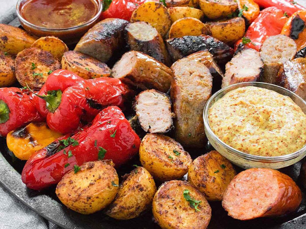 Angled view of a platter of grilled sausages, peppers, and potatoes.