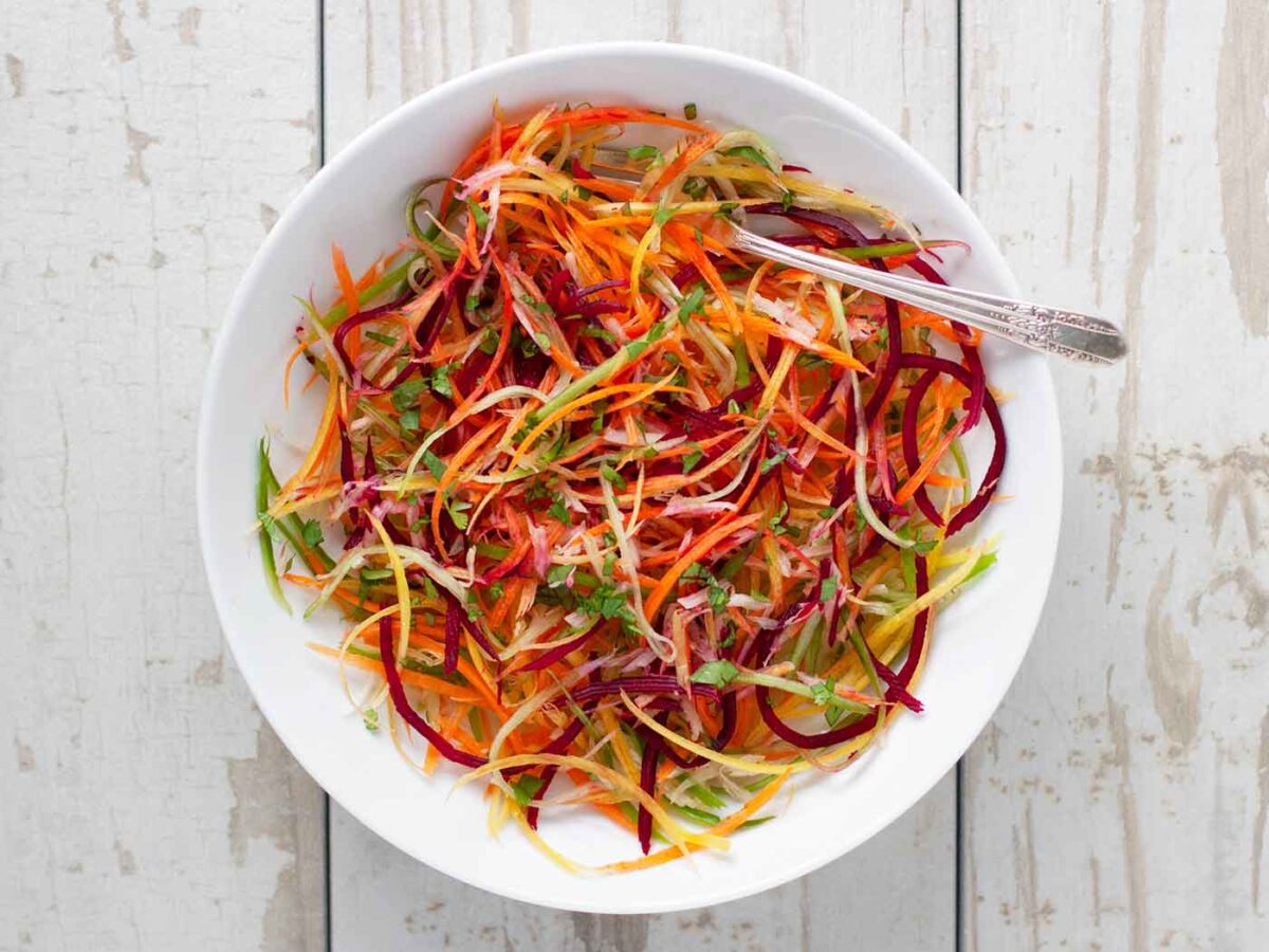 Rainbow Ribbon Veggie Salad in a white bowl with a serving spoon.