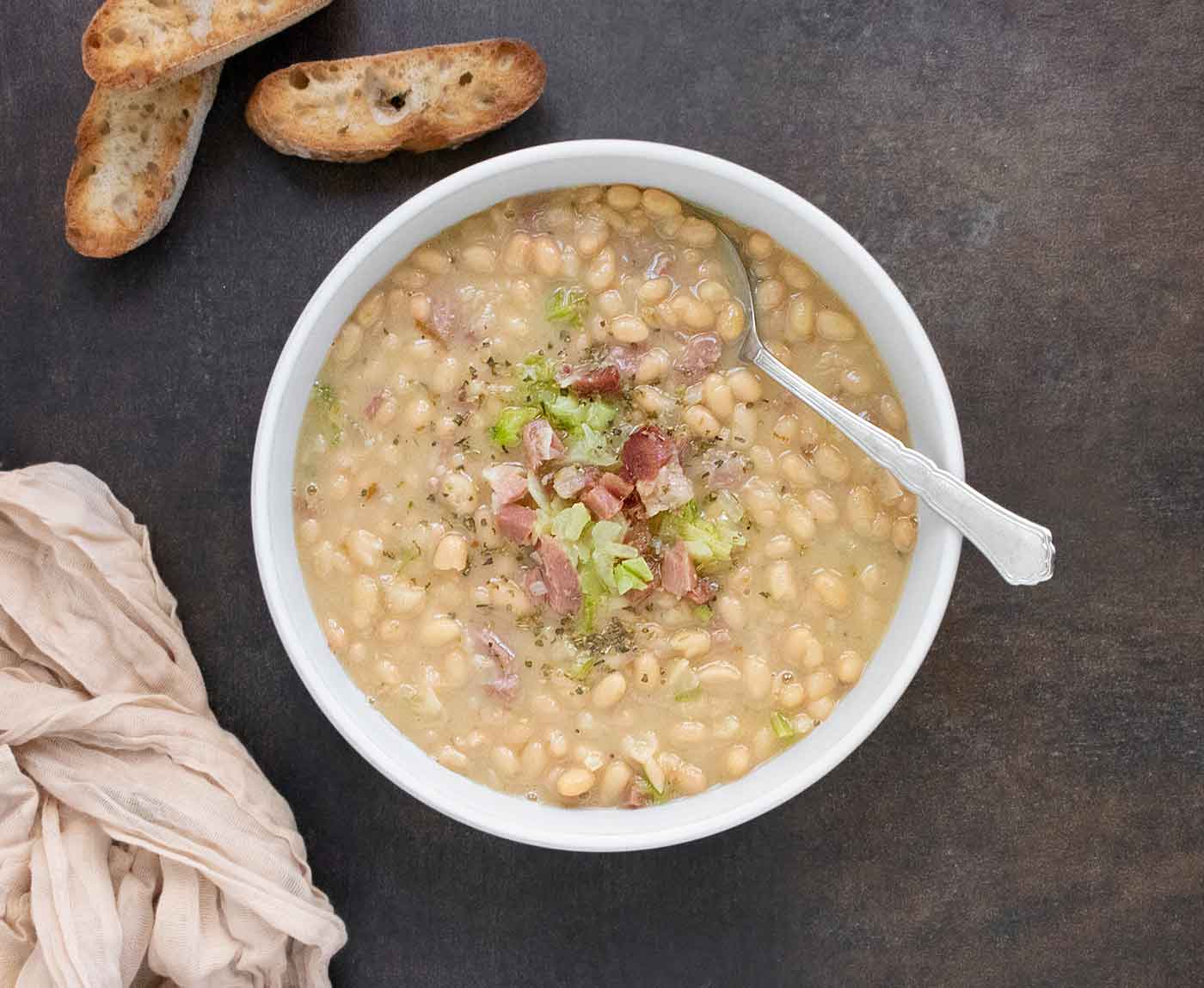 Senate Bean Soup in a white bowl with a spoon, and slices of bread on the side.